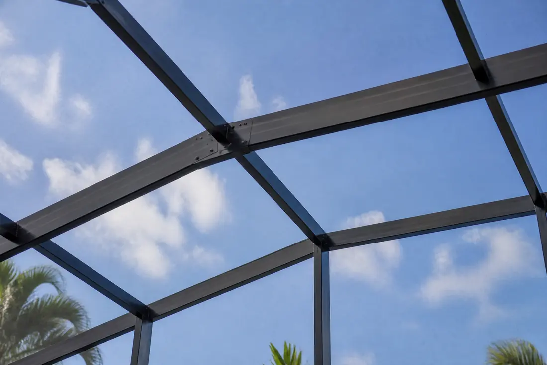 Aluminum framing of a screened pool enclosure seen from below against the sky