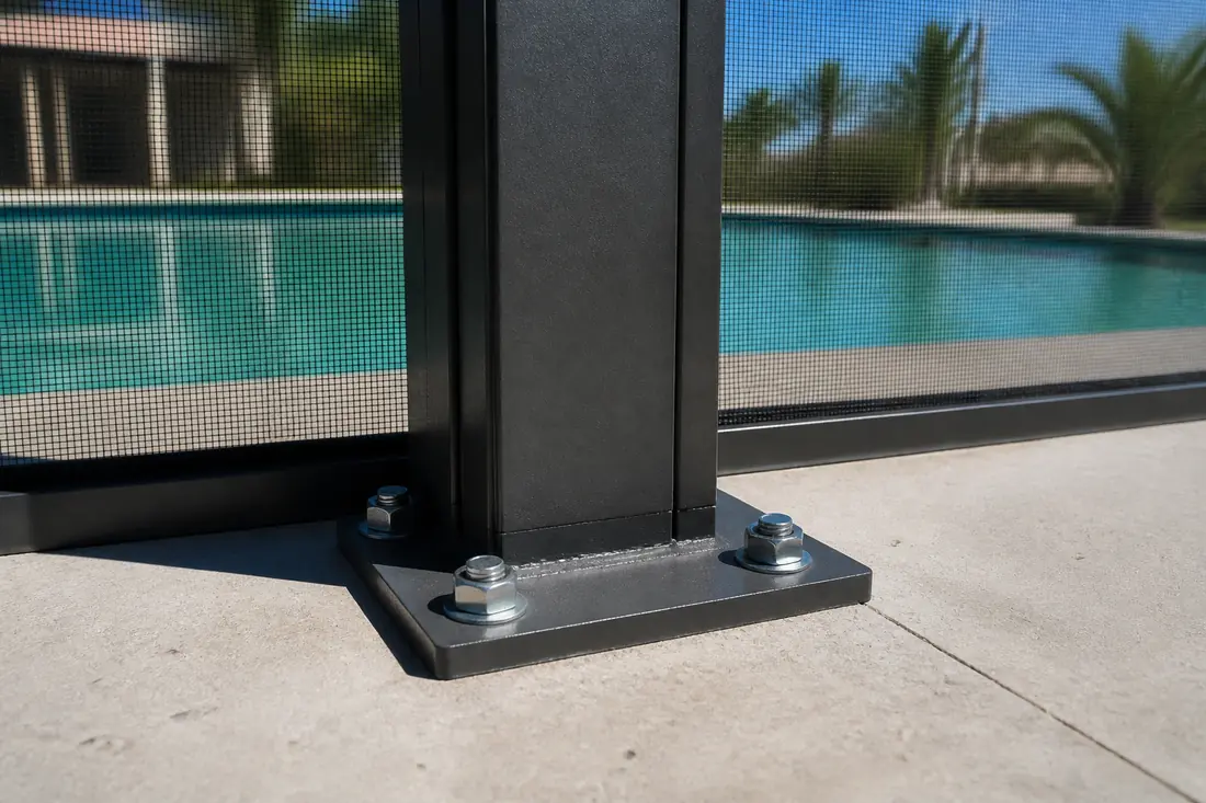 The base of a pool cage upright bolted down to a concrete deck beside a pool